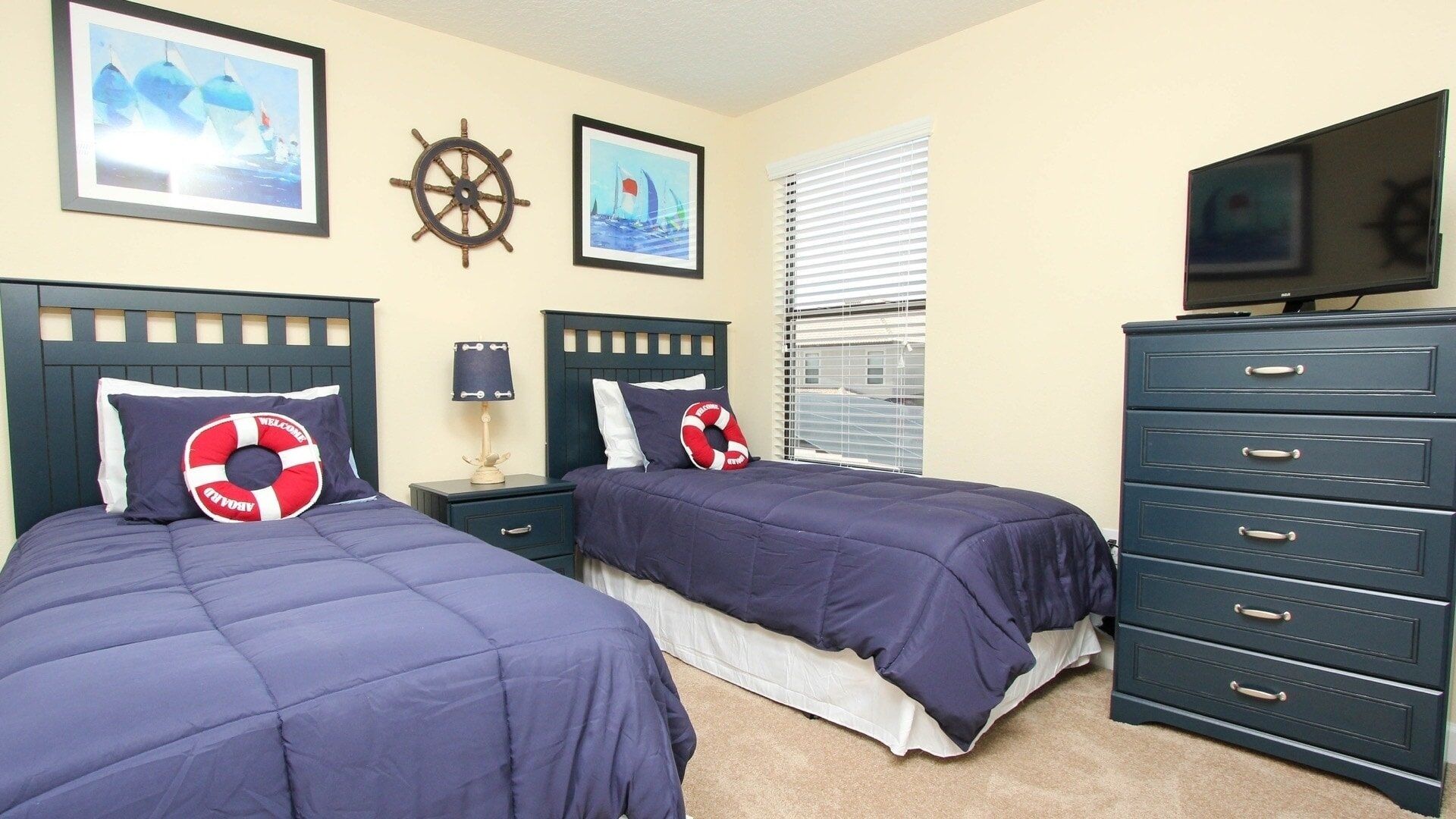 A hotel room with two beds, a dresser, a TV, and nautical-themed decor.