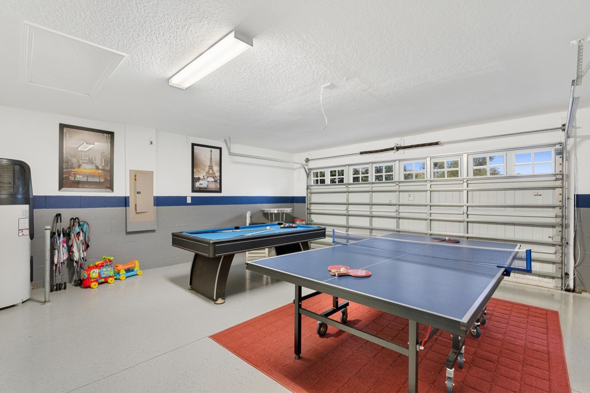 A room with a ping pong table, a pool table, and a garage with a car.