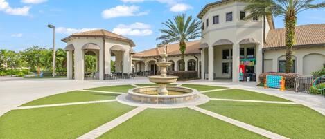 A courtyard with a fountain, outdoor seating, and a building with arches and a tiled roof.