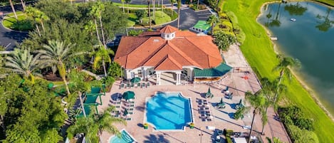 Vista aérea de un resort con piscina, sillones de descanso y una zona ajardinada con palmeras.