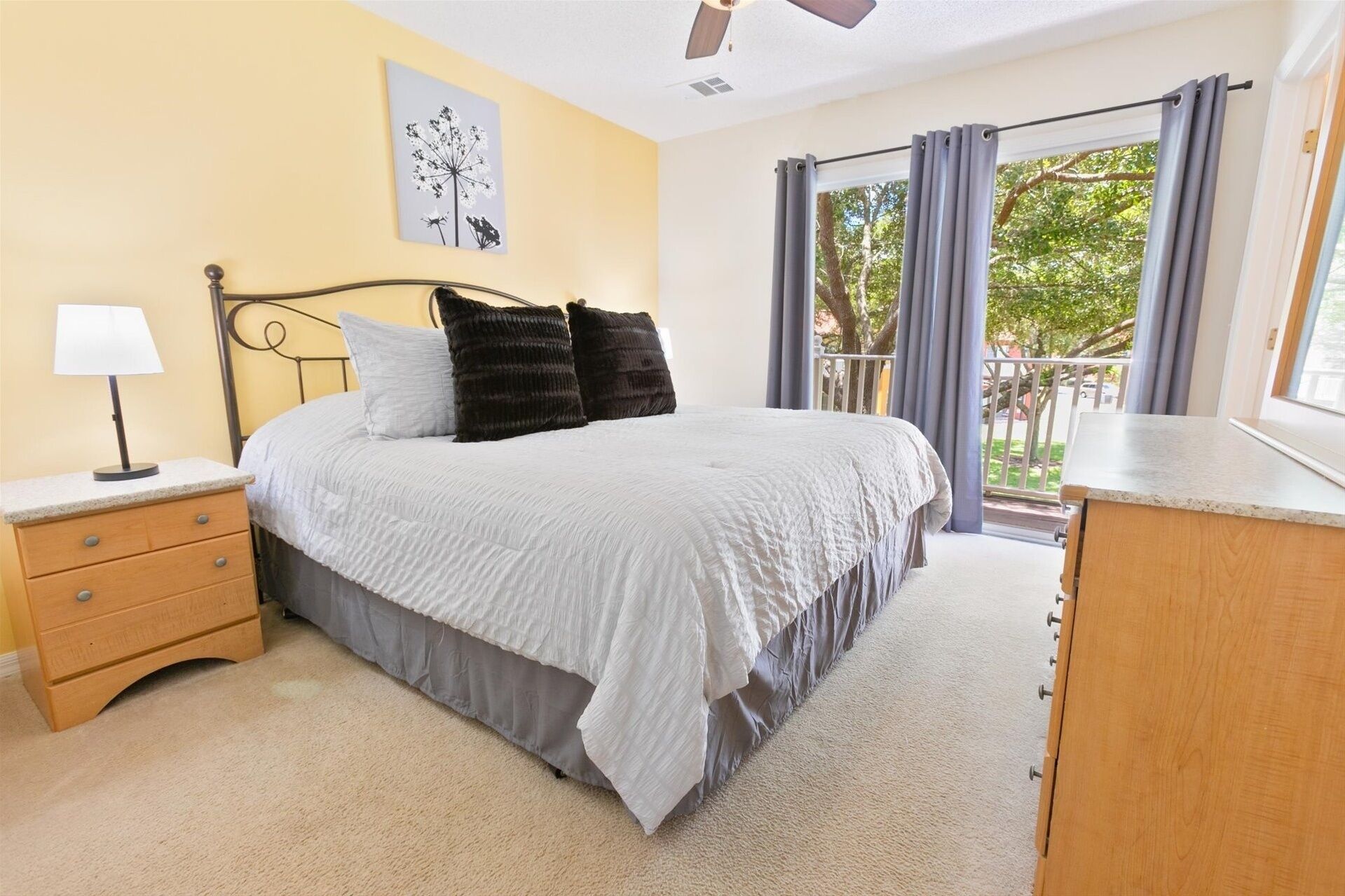 A bedroom with a bed, nightstand, lamp, and a view of the outdoors through large windows.