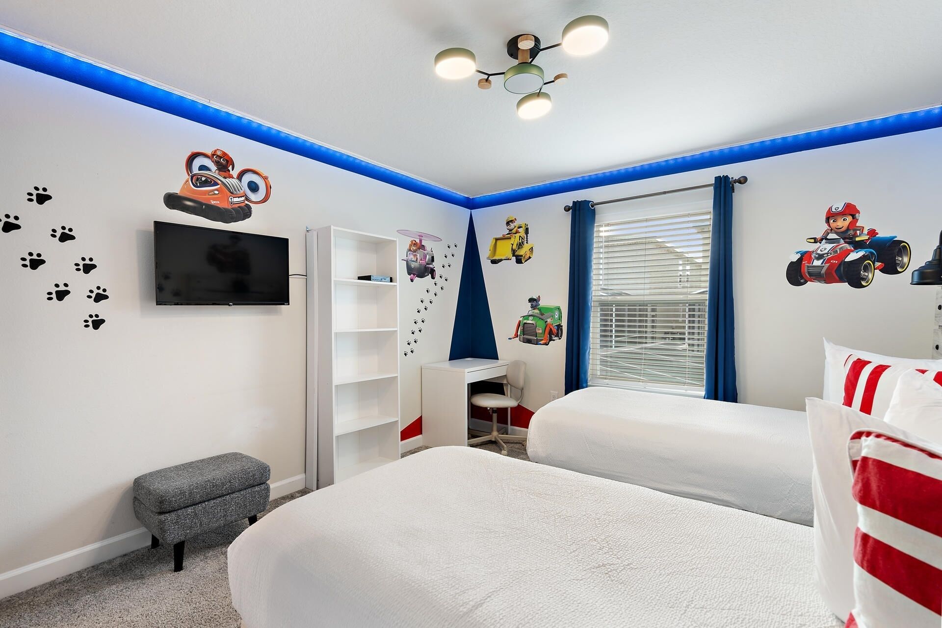 A bedroom with two beds, a TV, a desk, and wall decals.