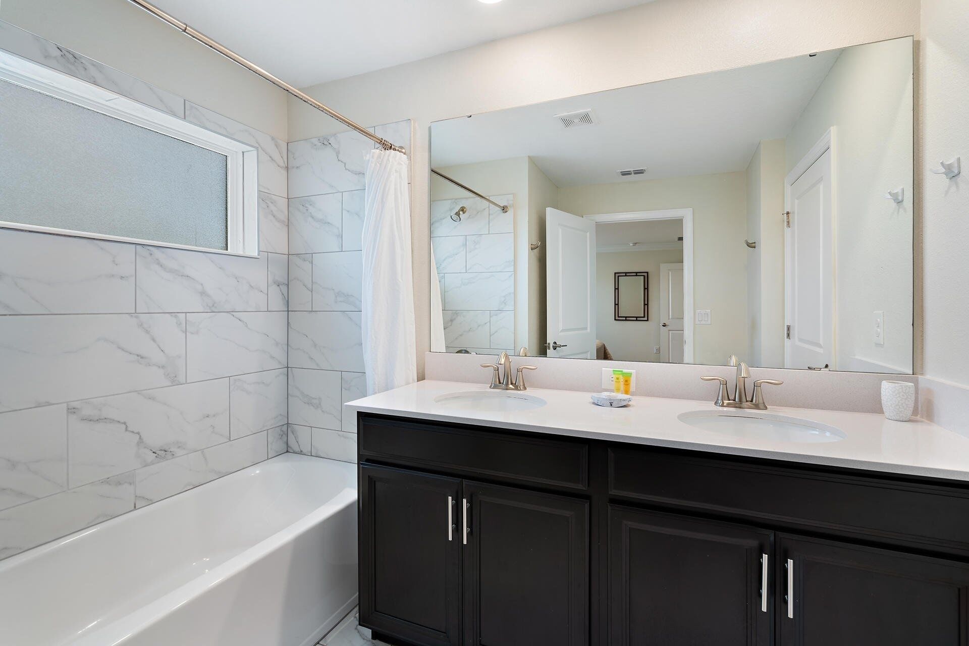 Une salle de bain moderne avec une baignoire, deux lavabos, un grand miroir et des meubles de rangement aux couleurs sombres.