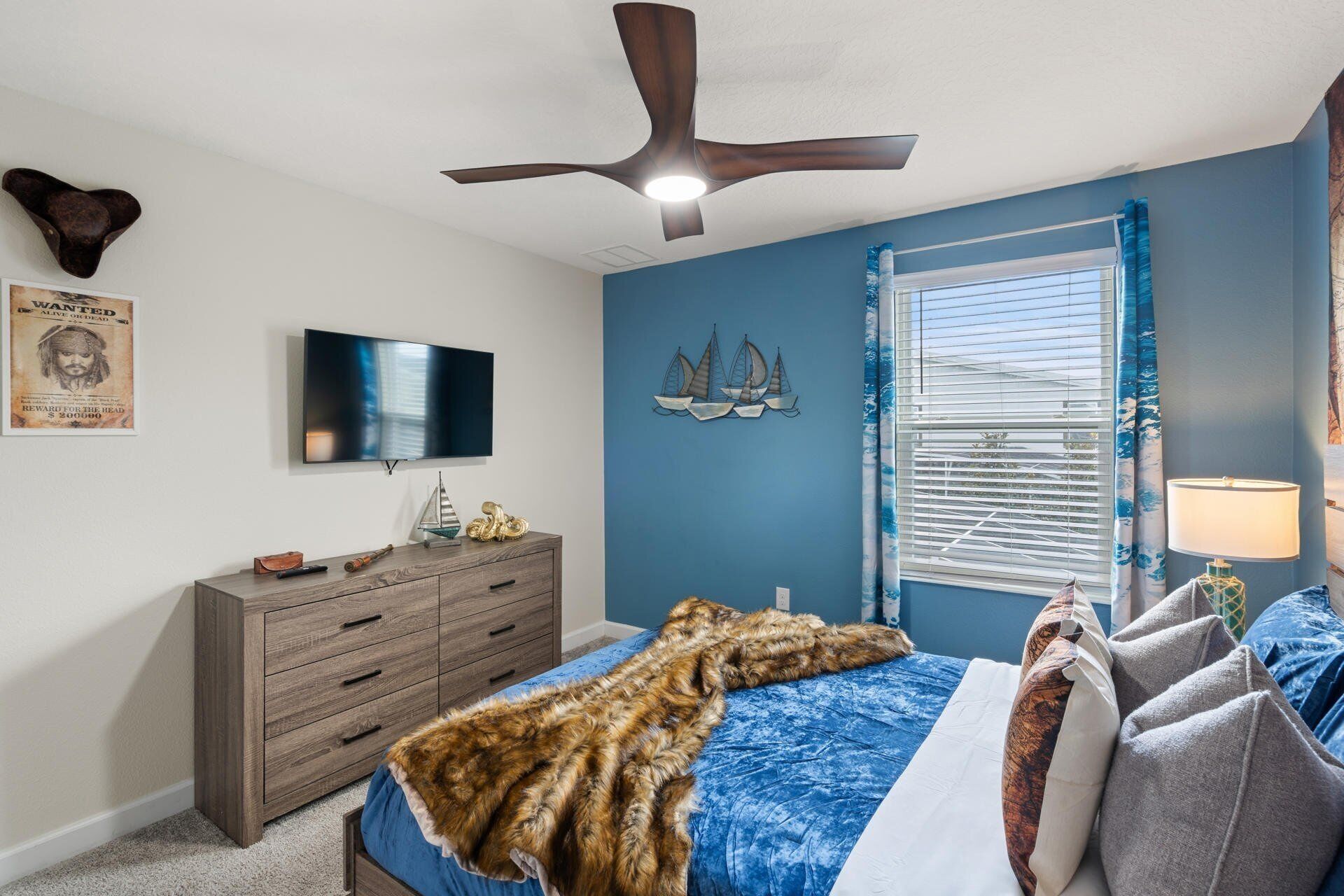 A bedroom with a bed, a dresser, a TV, a ceiling fan, and a window with blinds.