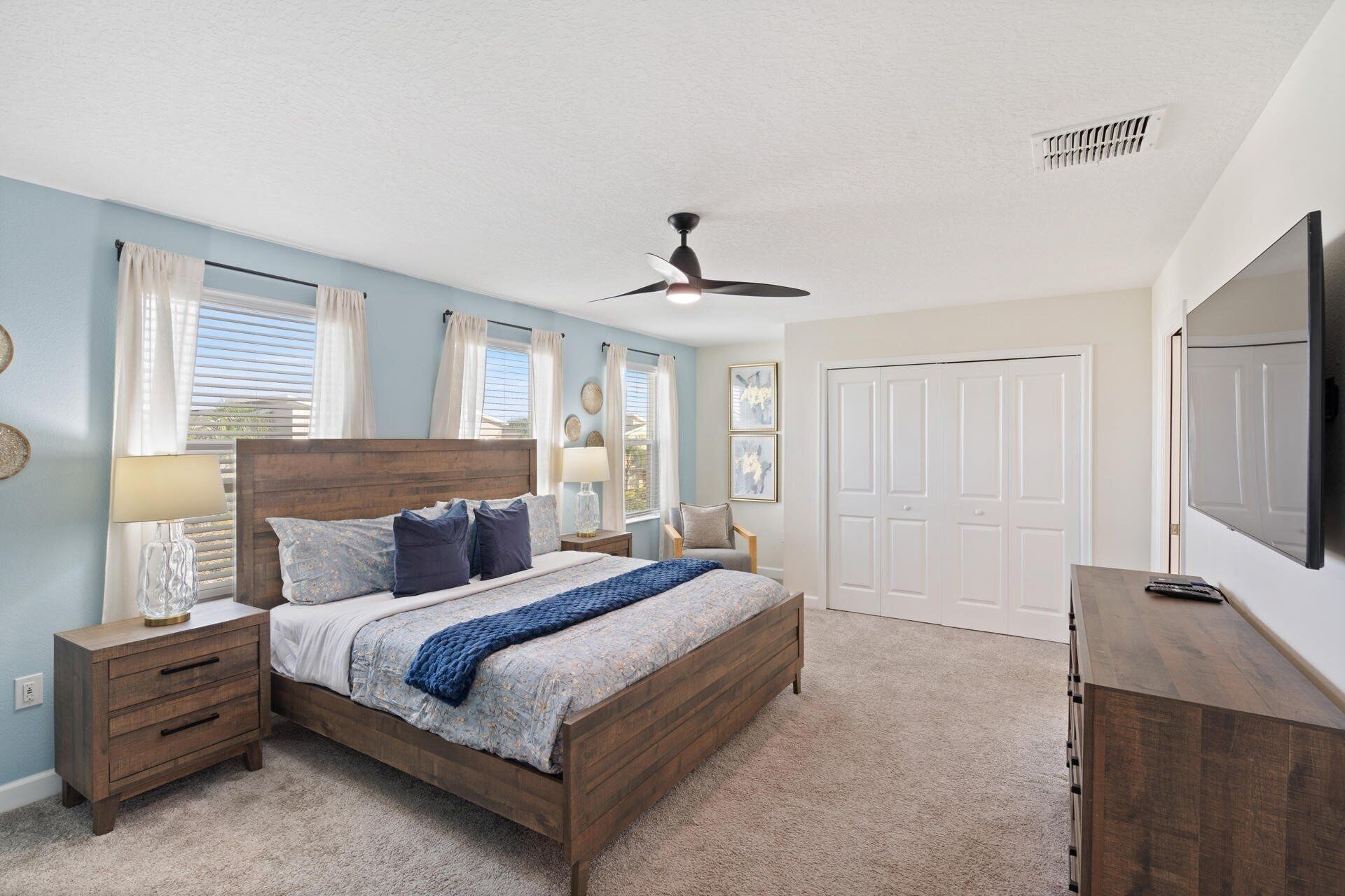A bedroom with a wooden bed, a ceiling fan, a TV, and a door.