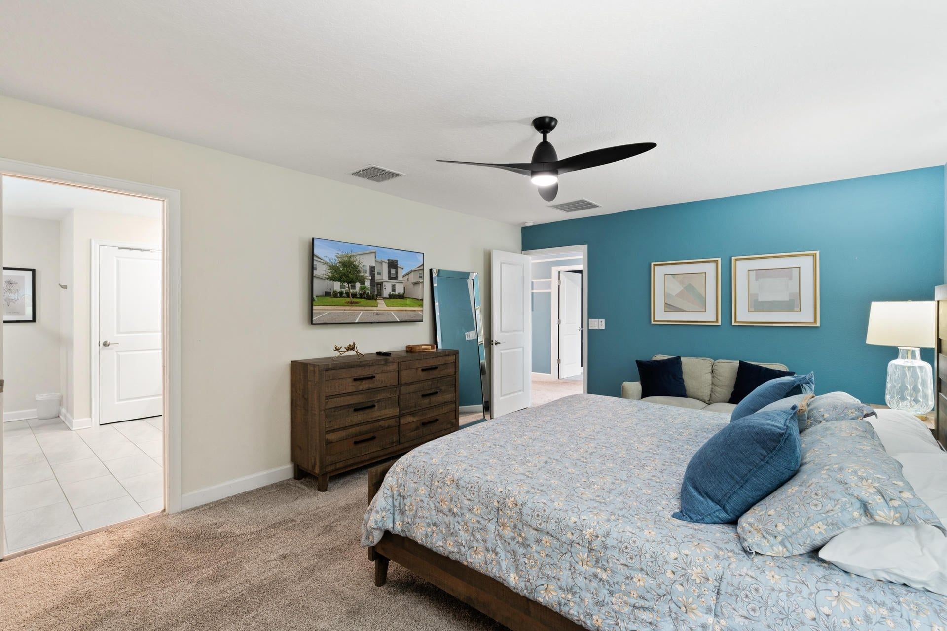 A bedroom with a bed, dresser, ceiling fan, and artwork on the wall.
