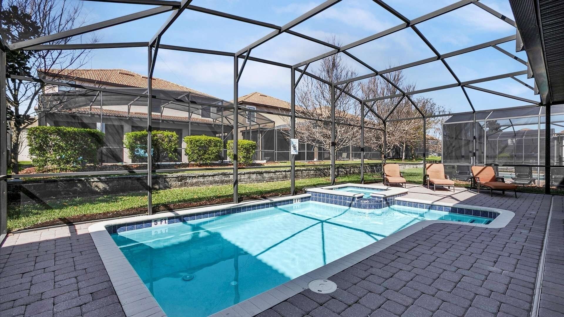 A covered outdoor swimming pool with a clear view of the surrounding area, including a brick patio and lounge chairs.