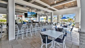 Un espace extérieur aménagé pour les repas, avec des tables et des chaises, un bar et une piscine en arrière-plan.