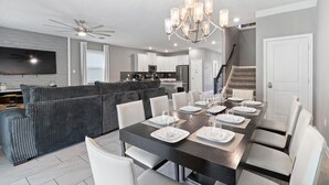 Un salon moderne avec une table à manger en bois foncé, dressée pour six personnes, un canapé gris et un ventilateur de plafond.