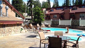 A pool area with lounge chairs and a table, surrounded by stone walls and a stone building. - Chamonix 33: Close to Canyon Lodge (Mammoth Lakes)