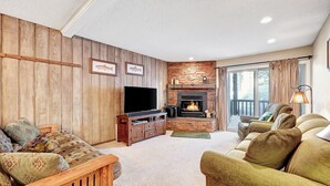 A cozy living room with a fireplace, wooden paneling, a large TV, and comfortable seating. - Chamonix 33: Close to Canyon Lodge (Mammoth Lakes)