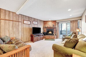 Ein gemütliches Wohnzimmer mit Kamin, Holzvertäfelung, einem großen Fernseher und bequemen Sitzmöglichkeiten.