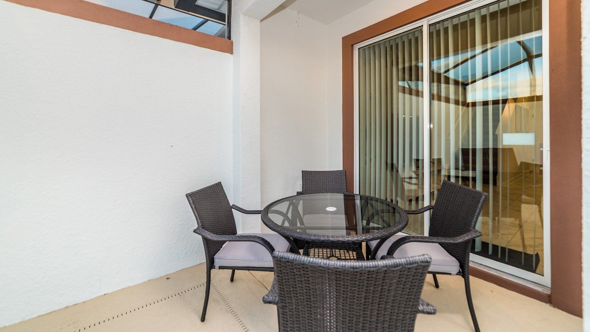 A glass-top table with four wicker chairs, a sliding glass door, and a white wall.