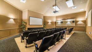 Ein Konferenzraum mit Tischen und Stühlen, einer großen Leinwand und einem Projektor.
