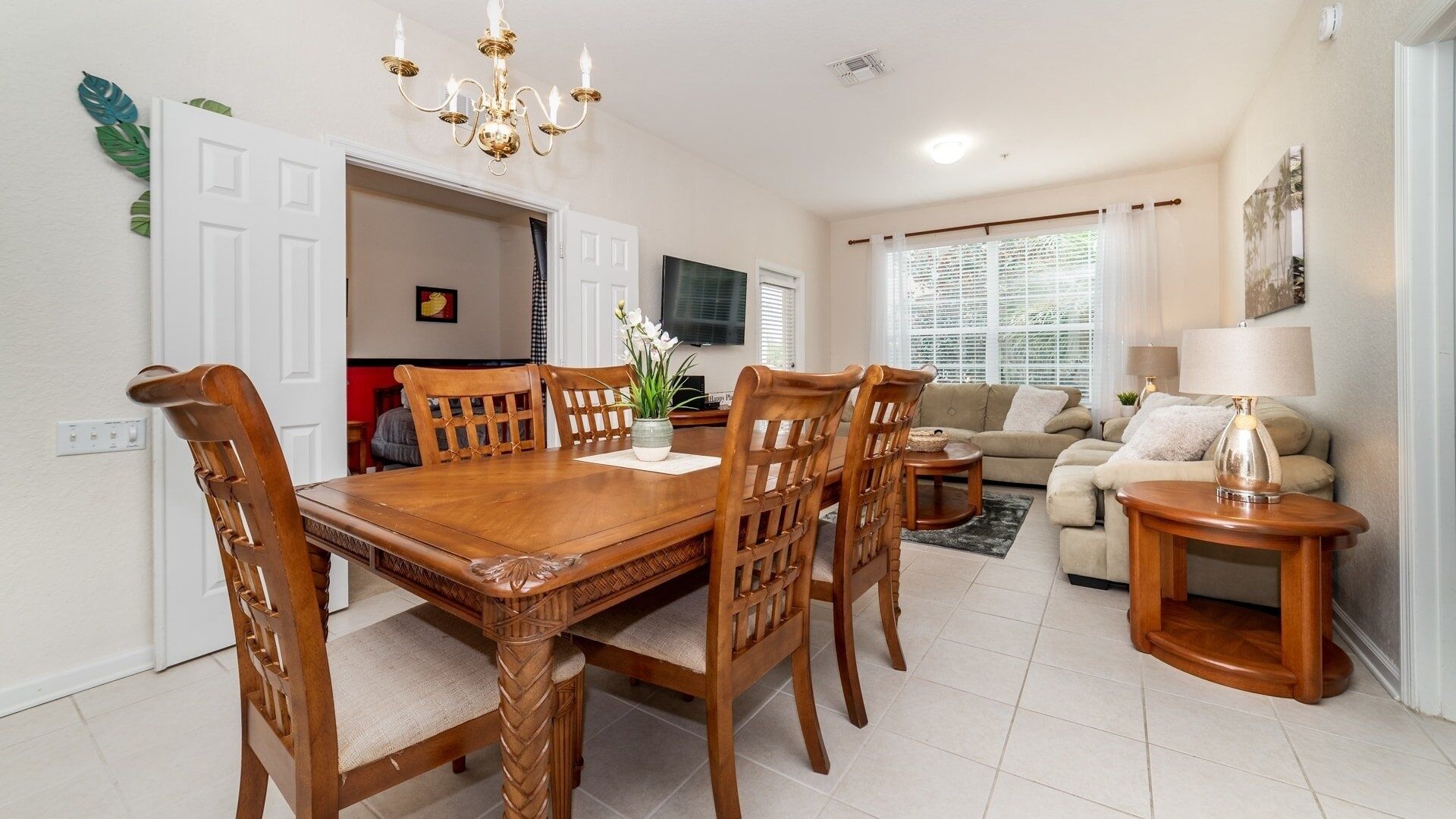 A dining area with a wooden table and chairs, a chandelier, and a television in the background.