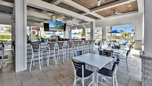 A covered outdoor dining area with multiple tables and chairs, a bar area with a TV screen, and a pool visible through the open sides. - Championsgate Resort 5 Bedroom Private Pool Home 5 Home (Davenport)