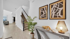 A modern interior with a staircase, a potted plant, and two abstract paintings. - Championsgate Resort 5 Bedroom Private Pool Home 5 Home (Davenport)
