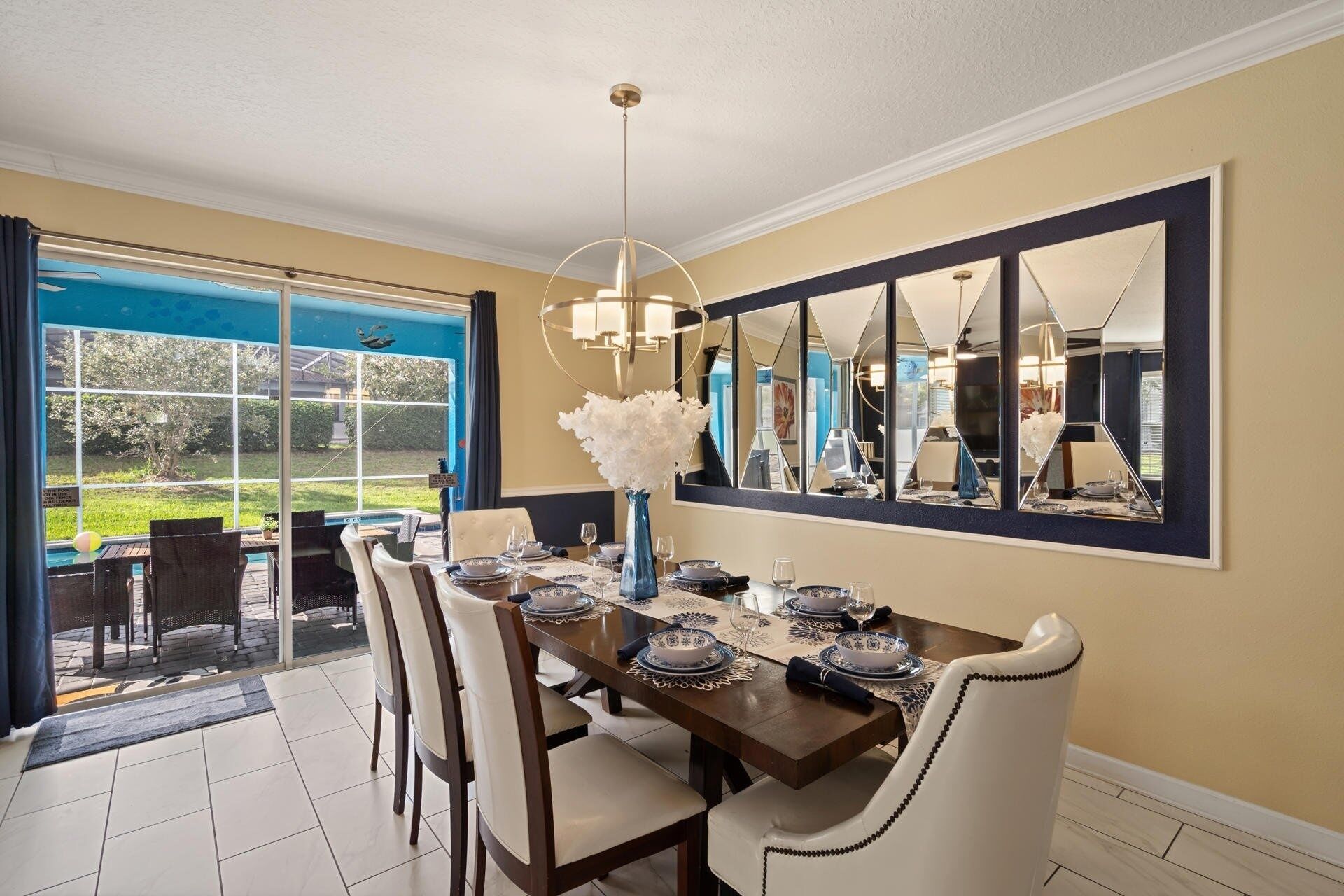 Une salle à manger avec une grande table dressée pour six personnes, un vase décoratif et un grand miroir au mur.