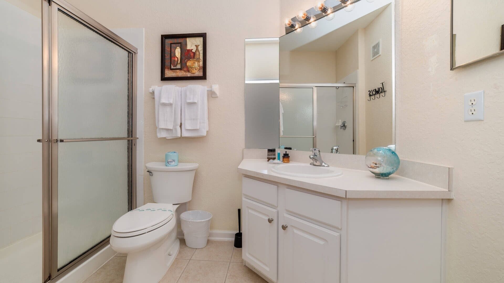 A bathroom with a toilet, sink, cabinet, and a glass shower enclosure.