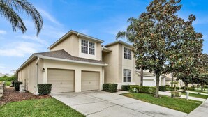 A two-story residential house with a beige exterior, two garage doors, and a well-maintained lawn. - Windsor Hills Resort 5 Bedroom Updated Pool Home 5 Home (Kissimmee)