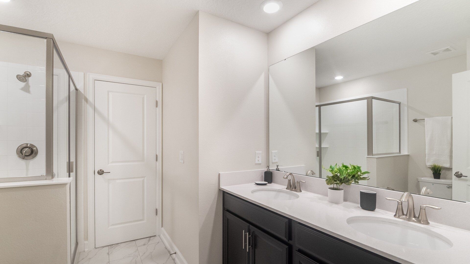 A modern bathroom with two sinks, a large mirror, and a shower area.