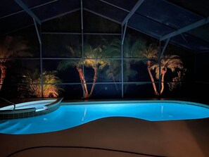 A swimming pool with a curved edge, surrounded by palm trees and a glass enclosure. - 4 Bedroom Private Pool+Spa Home 8 Miles to Disney 4 Home (Kissimmee)