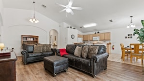 A spacious living room with leather sofas, a wooden coffee table, and a dining area with wooden chairs. - 4 Bedroom Private Pool+Spa Home 8 Miles to Disney 4 Home (Kissimmee)