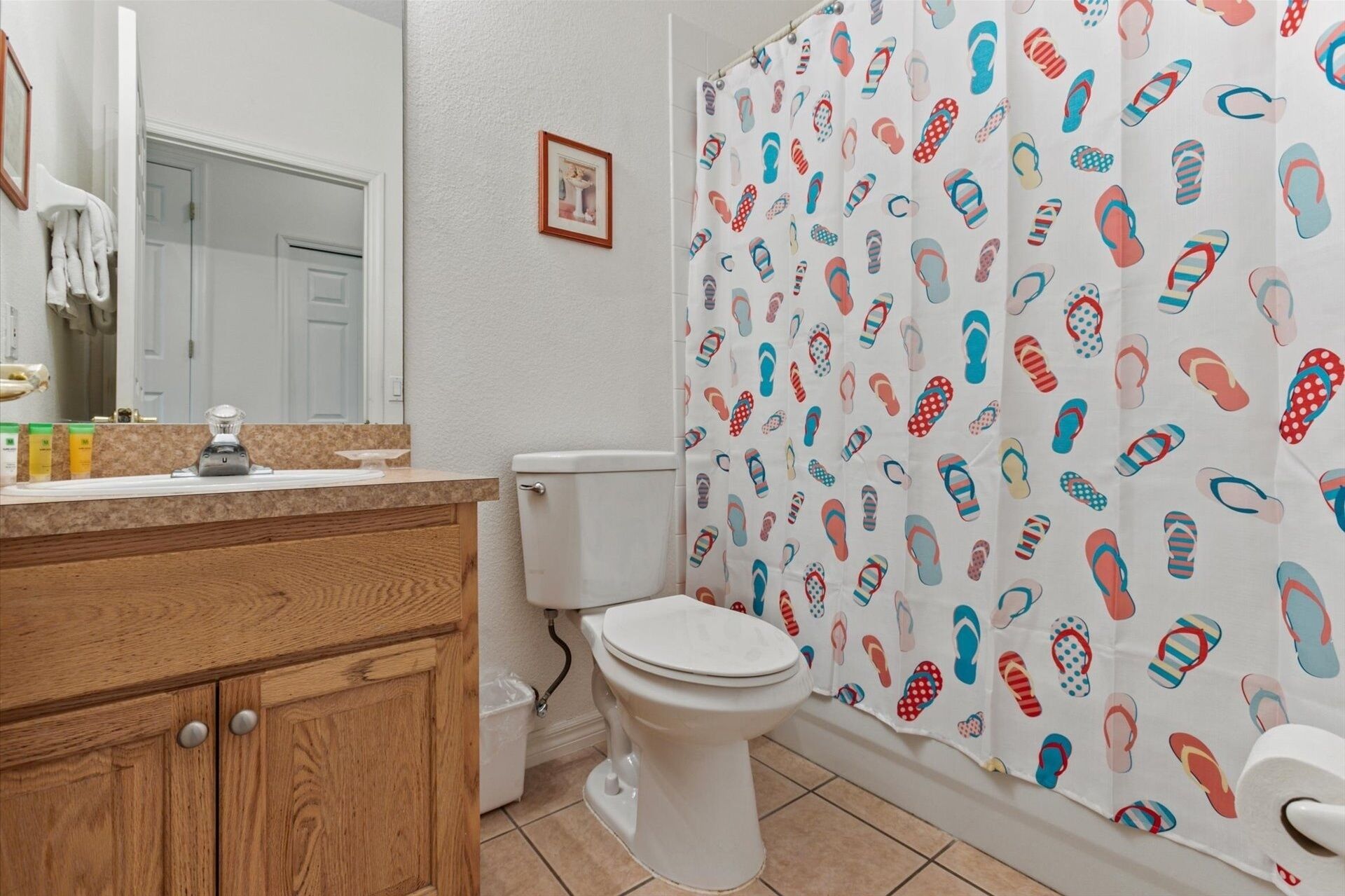 A bathroom with a wooden vanity, a toilet, and a shower curtain with a flip-flop pattern.
