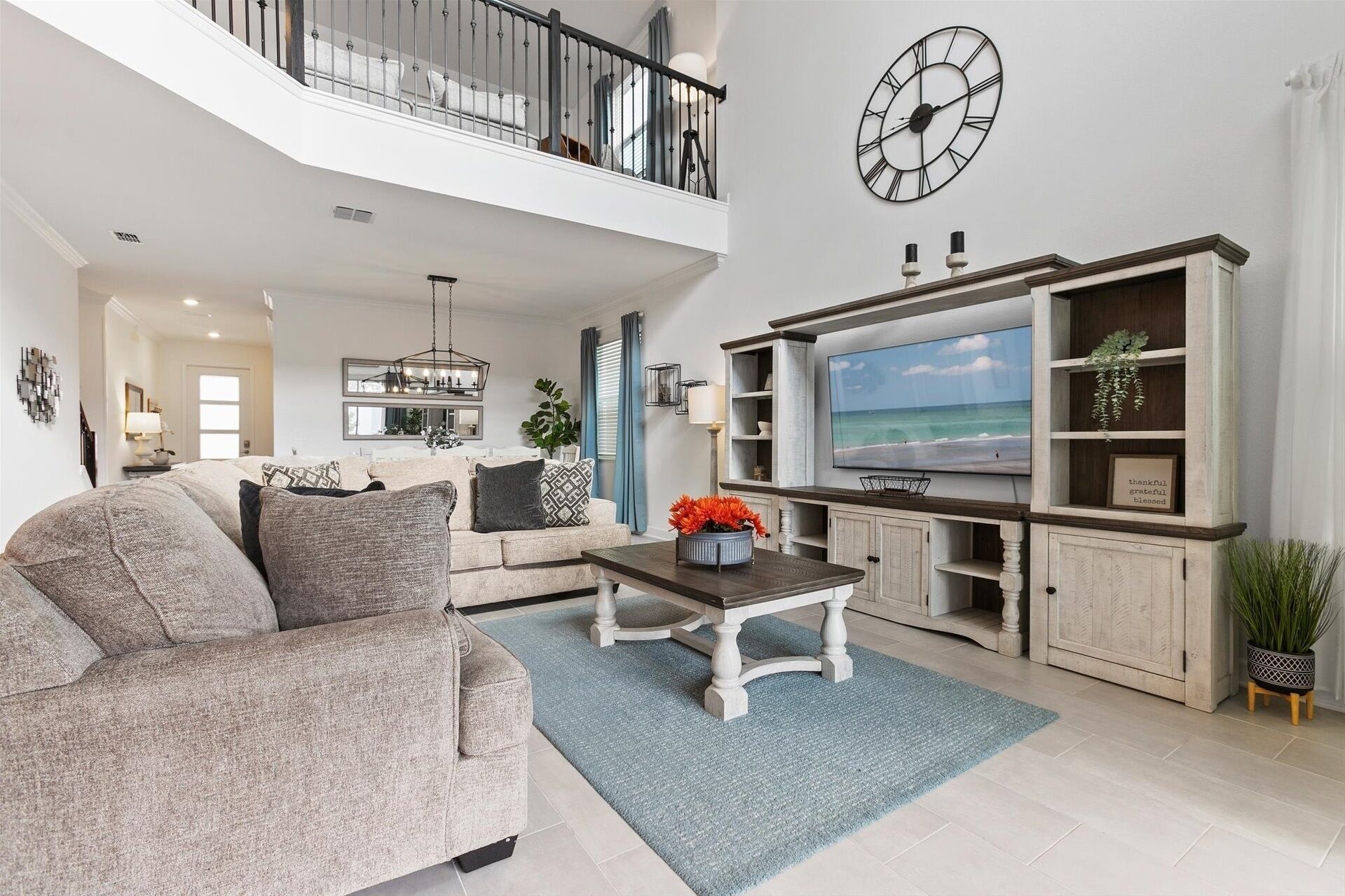 A spacious living room with a high ceiling, a large TV mounted on the wall, and a balcony with a railing.
