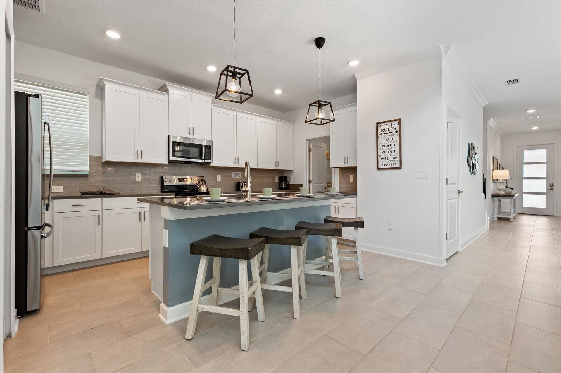 A modern kitchen with white cabinets, a central island with stools, a microwave, and a refrigerator.