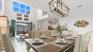 A spacious dining area with a high ceiling, large windows, and a modern chandelier. - Championsgate Resort 6 Bedroom Private Pool+Spa Home 5 Home (Davenport)