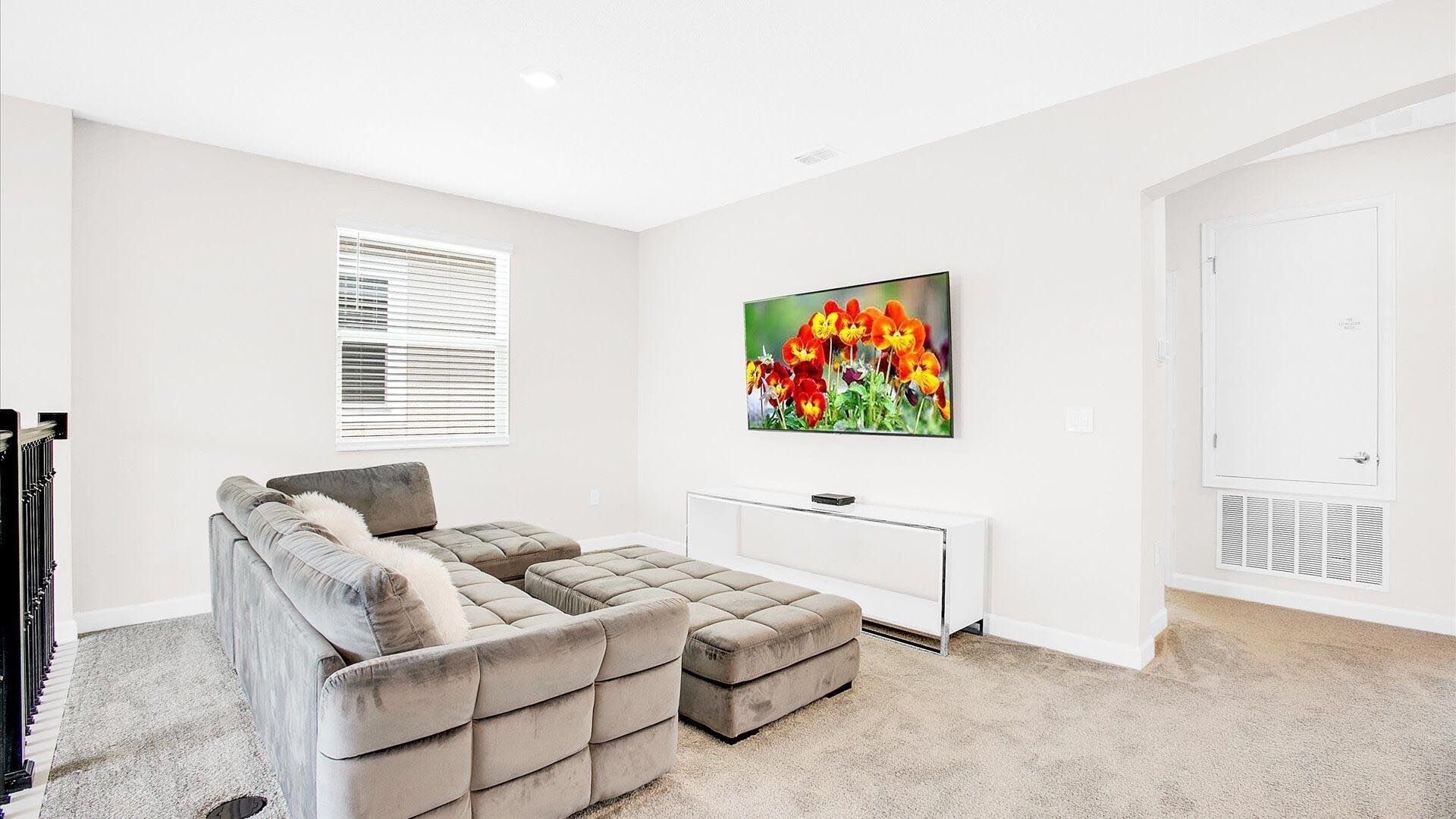 A living room with a sectional sofa, a flat-screen TV, a white console table, and a door with a vent.