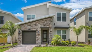 A modern two-story residential building with a stone facade, a garage, and a well-maintained lawn. - Championsgate Resort 5 Bedroom Private Pool Home 5 Home (Kissimmee)