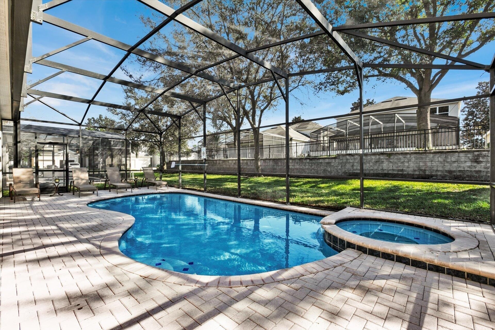 An indoor swimming pool with a glass enclosure, surrounded by a brick patio and equipped with lounge chairs.