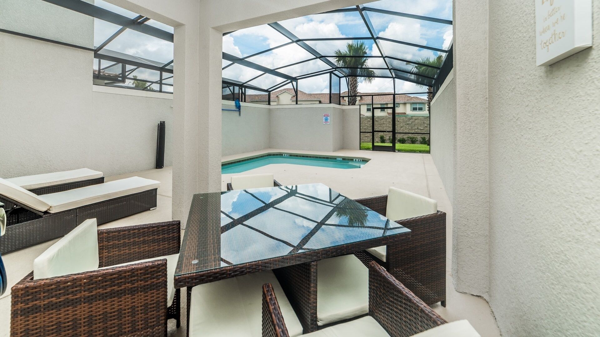 An outdoor patio with a glass-top table, wicker chairs, and a swimming pool.