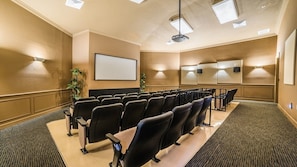 Uma sala de conferências com fileiras de cadeiras, uma tela grande e um projetor.