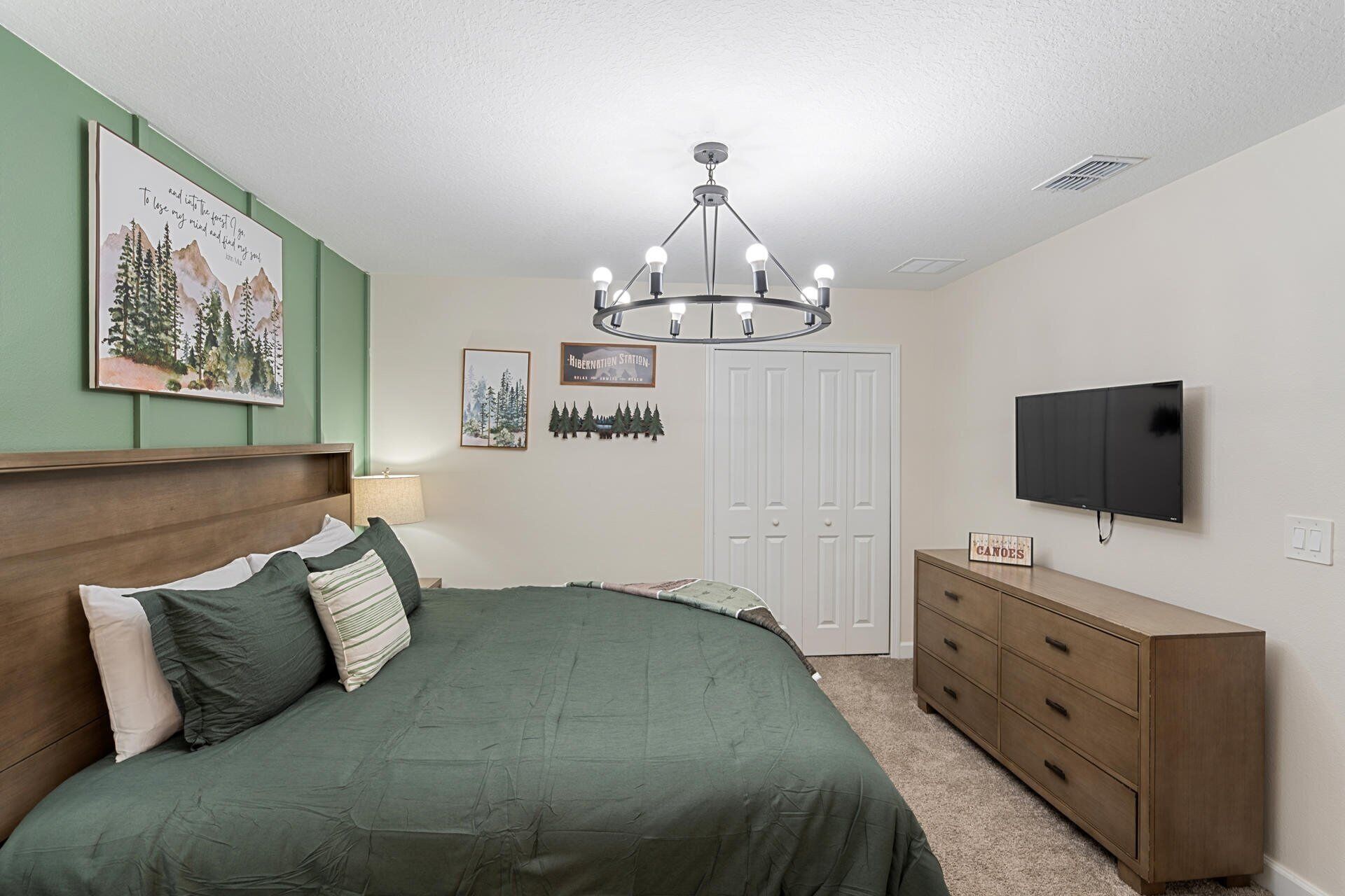 Quarto com cama, cômoda, televisão e lustre.