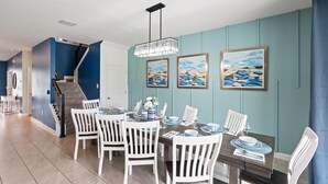 A dining area with a table set for four, white chairs, and a chandelier. - ChampionsGate Resort 10 Bedroom Vacation Home - Includes resort clubhouse amenity access! 10 Home (Davenport)