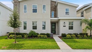 A two-story residential building with a stone chimney, multiple windows, and a well-maintained lawn. - ChampionsGate Resort 10 Bedroom Vacation Home - Includes resort clubhouse amenity access! 10 Home (Davenport)