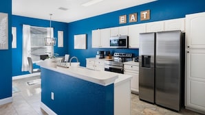 A modern kitchen with a blue accent wall, white cabinetry, a stainless steel refrigerator, and a built-in oven. - Windsor Hills Resort 5 Bedroom Home with Game Room 5 Home (Kissimmee)