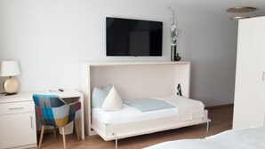 A modern bedroom with a bed, a desk, a chair, and a TV mounted on the wall. - Altstadt-Apartment (Freiberg)