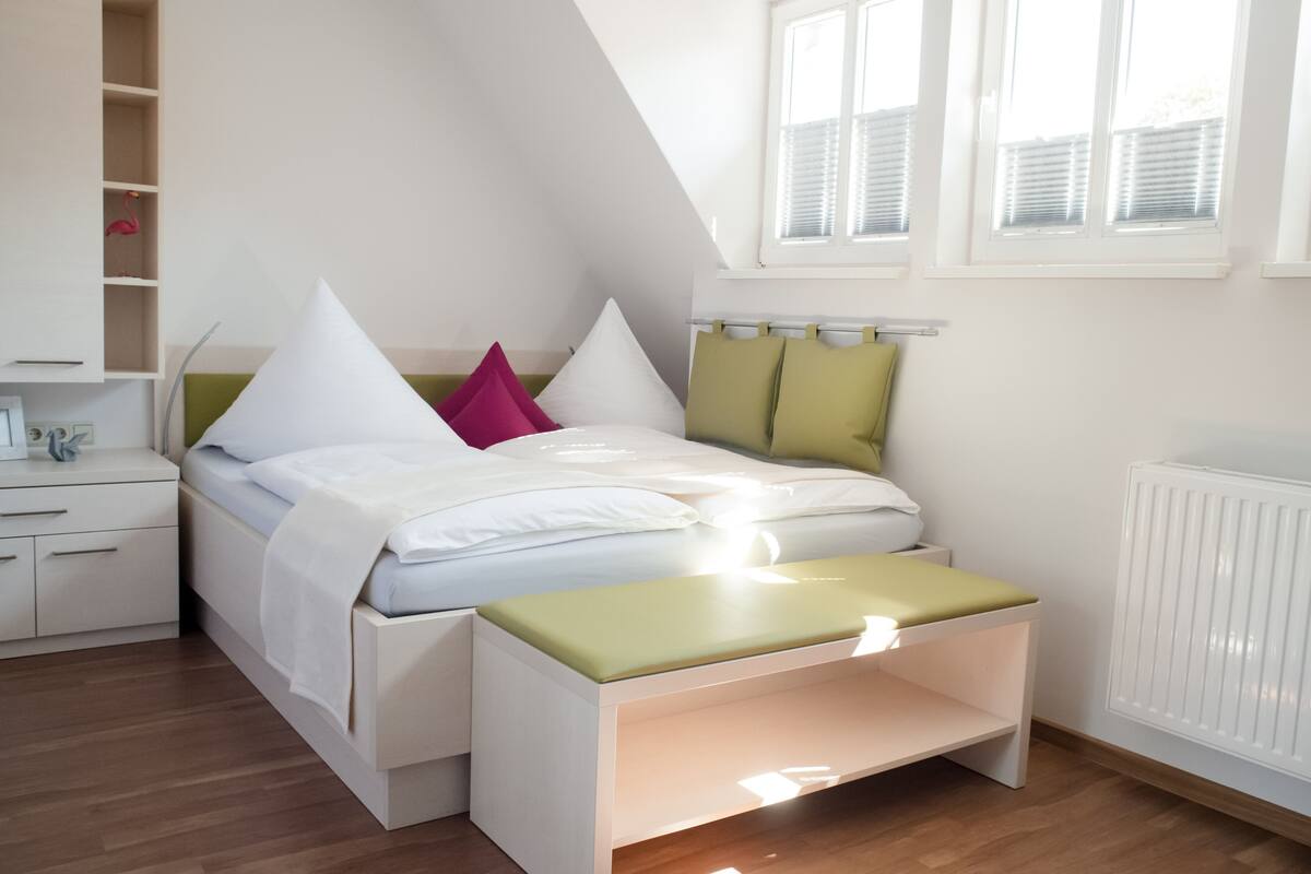 A modern bedroom with a bed, bedside tables, a bench, and a radiator.