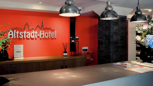 A hotel reception desk with a red wall, black pendant lights, and a city skyline graphic. - Altstadt-Apartment (Freiberg)