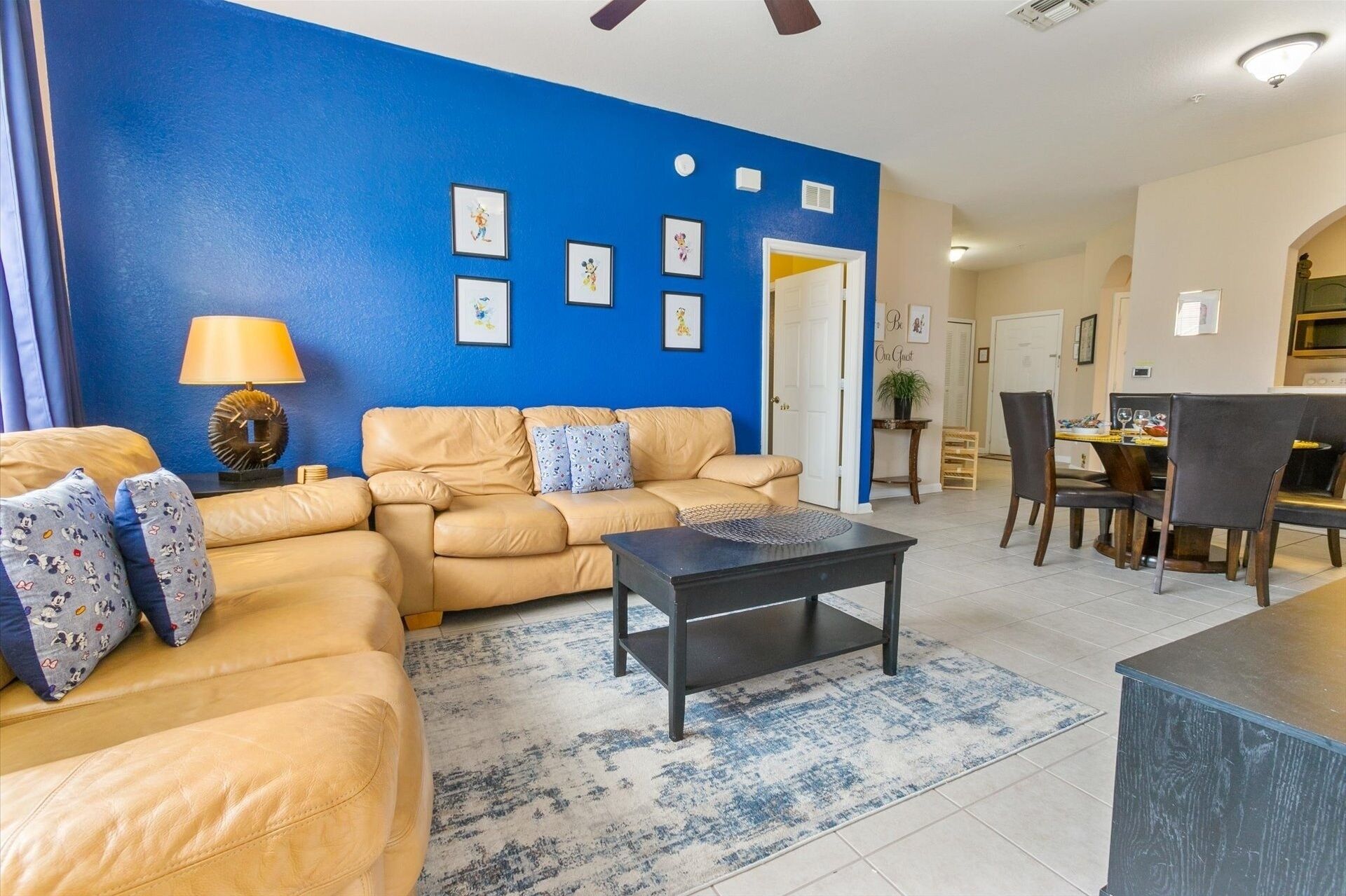 A living room with a blue accent wall, a sofa set, a coffee table, and a dining area with chairs and a table.