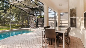 A covered outdoor pool area with a glass table and chairs, surrounded by a brick patio. - Windsor Hills Resort 6 Bedroom Home Incredible Game Room 6 Home (Kissimmee)