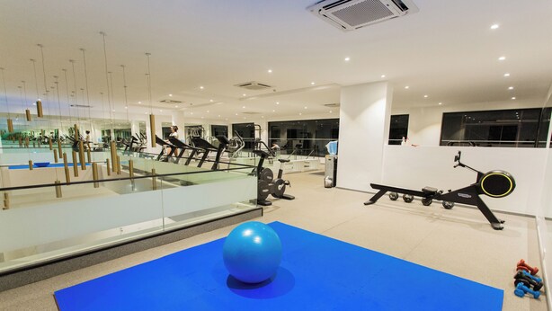 Ett modernt gym med träningsutrustning, en stor blå matta och en glasvägg som reflekterar interiören.