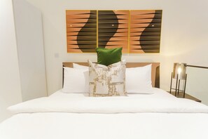 Ein Hotelzimmer mit einem ordentlich bezogenen Bett, einem modernen abstrakten Gemälde an der Wand und einem Nachttisch mit einer Lampe.