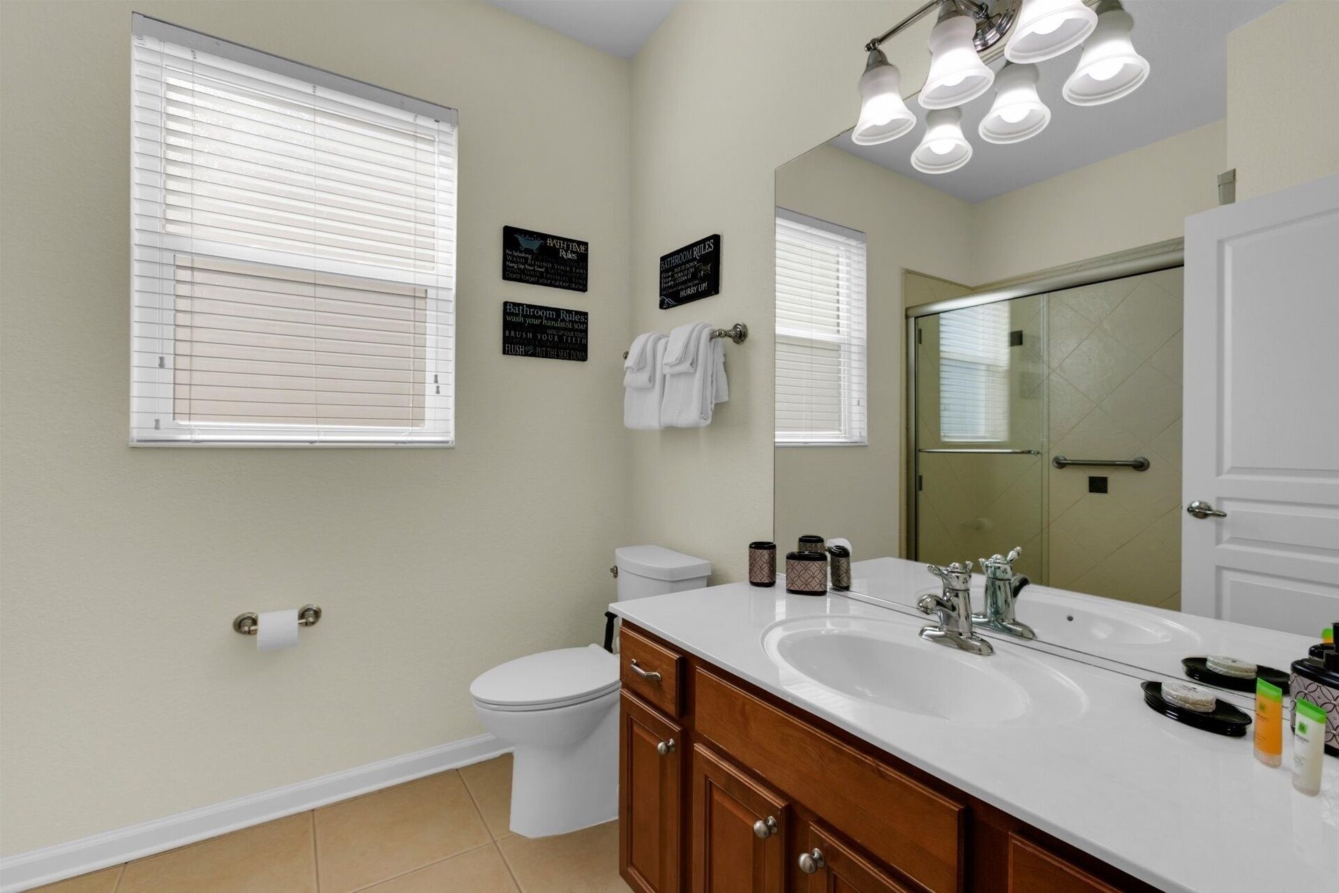 A bathroom with two sinks, a toilet, and a mirror. There are two signs on the wall with bathroom rules.