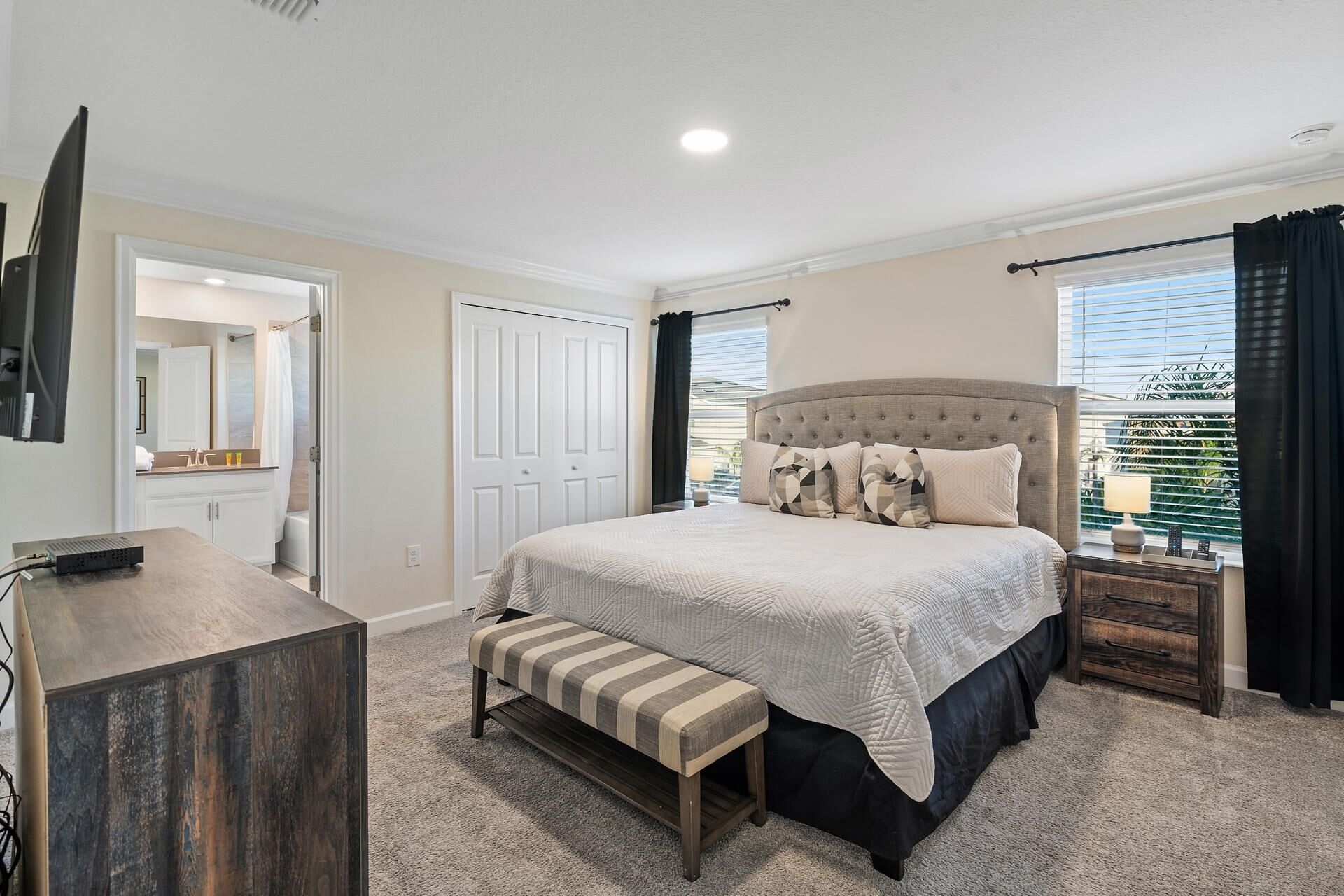 Een slaapkamer met een groot bed, een bankje, een dressoir en een raam met gordijnen.