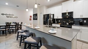 Une cuisine moderne avec des meubles blancs, un réfrigérateur noir, une cuisinière noire et un grand îlot central doté de tabourets de bar.